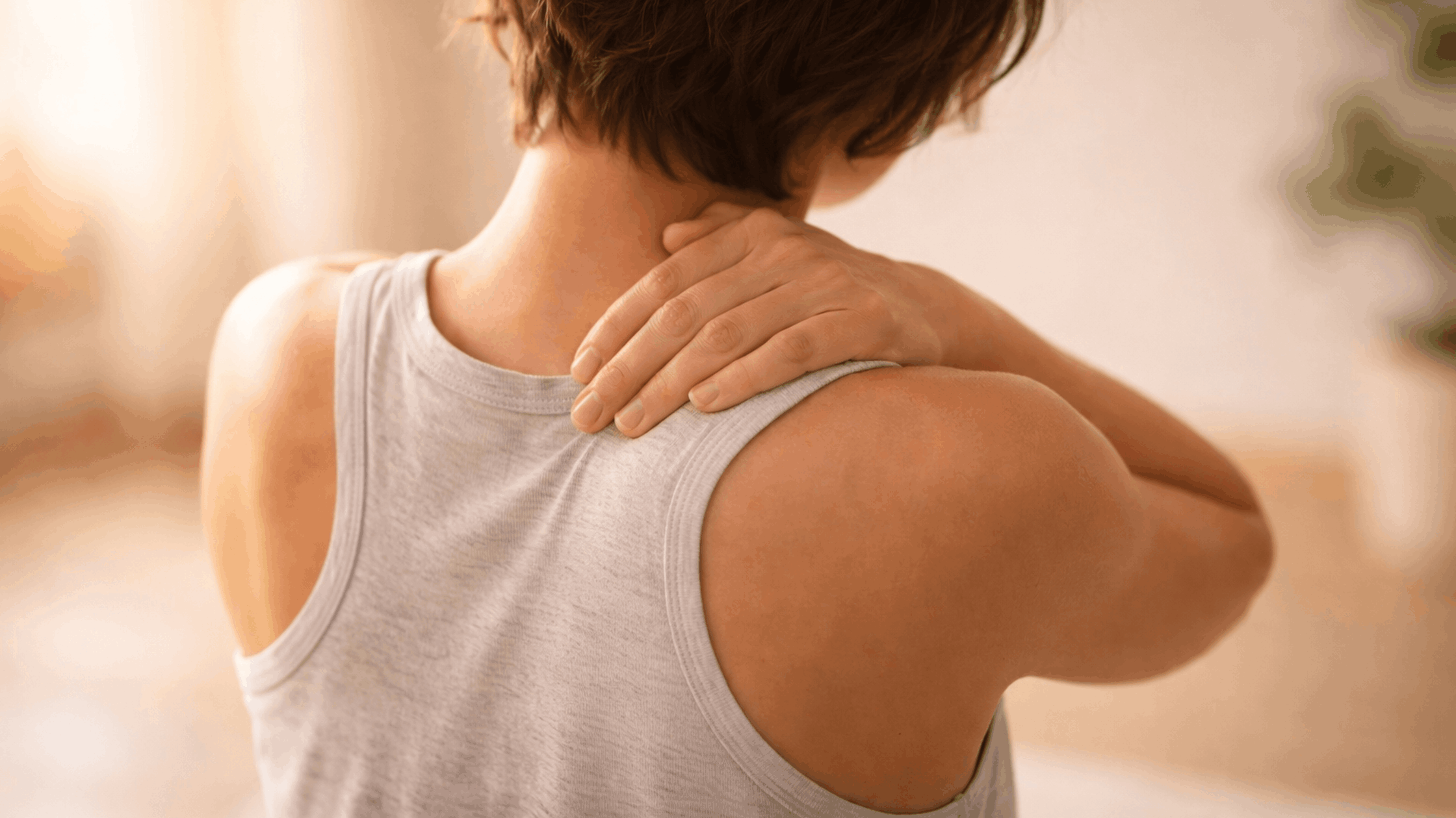Person with a back pain, holding their arm and shoulder against a blurred background